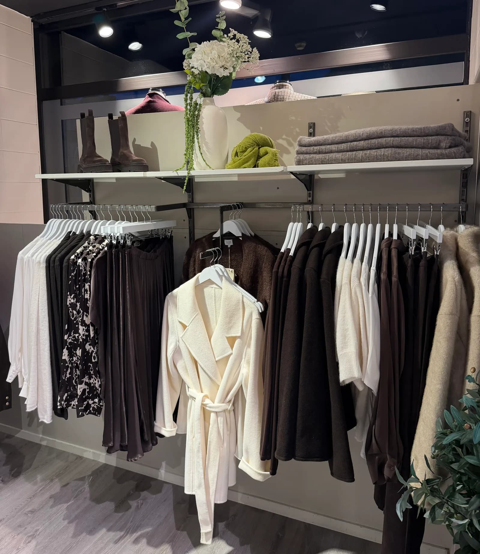 Kleskolleksjon på stativ i butikken, med en hvit kåpe i midten