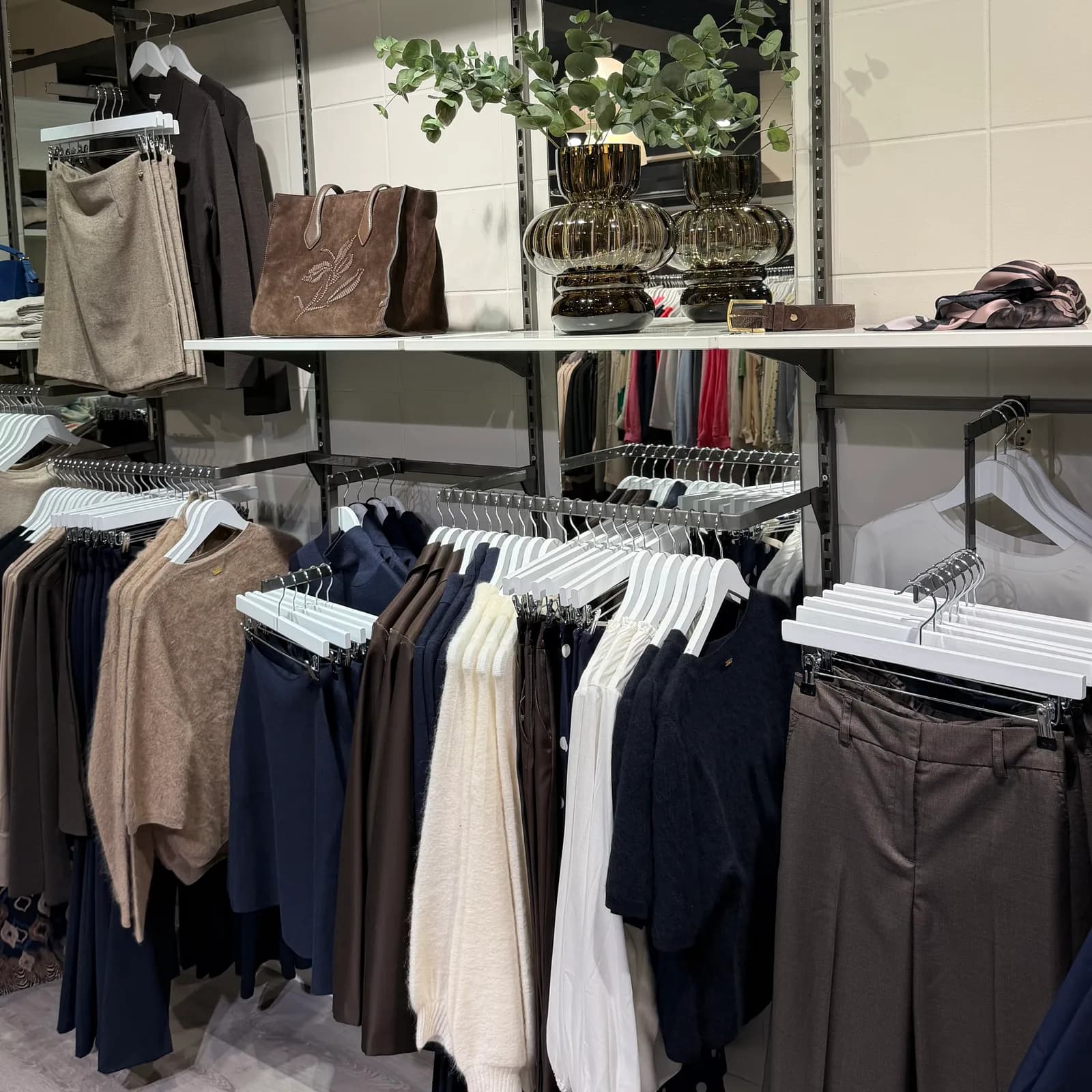 Klesstativ i butikken med strikk, skjørt og bukser i brune og blå toner